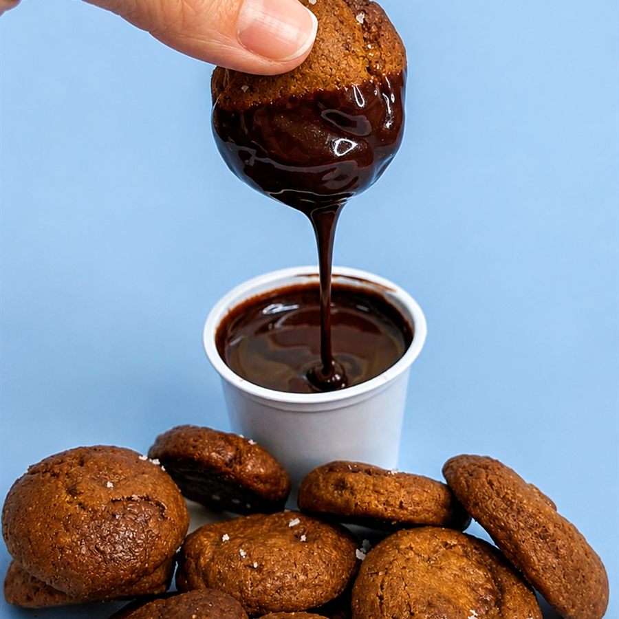 Mini cookies recheados sendo mergulhados na cobertura de chocolate